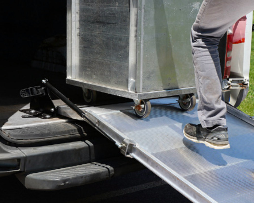 Cargo on wheels is pushed up a van ramp into the rear cargo area of a van